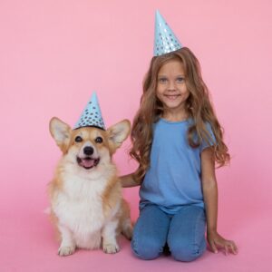 young-girl-and-corgi-dog-in-front-of-pink-background-wearing-birthday-party-hats