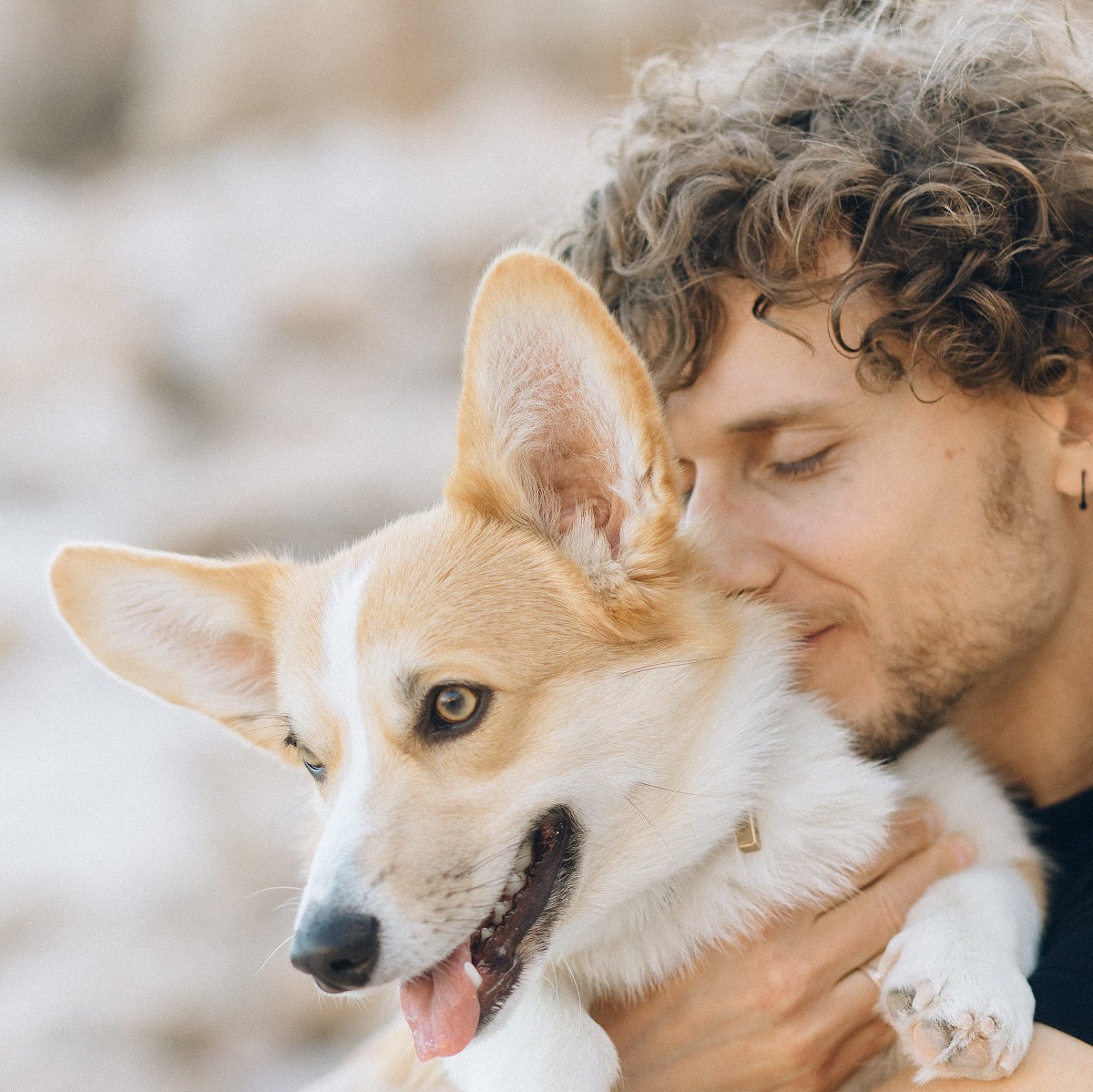 curly-haired-man-hugging-corgi-dog-outside